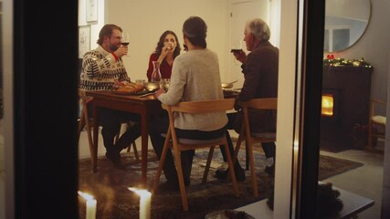 Wall Mural - European family sitting at dinner table toasting wine and having a Christmas eve dinner together. Family having thanksgiving dinner at home.
