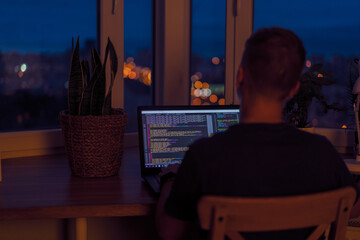 Wall Mural - a young male programmer in front of a window with a lights of night city, on his laptop screen is co