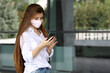 © vlarvix - Young beautiful woman with long hair, wearing protective face mask, looks through and scrolls something in her smartphone