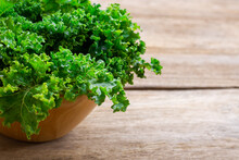 Closeup Fresh Green Curly Kale Cabbage Vegetable Leaves In Wooden Bowl Isolated On Wood Table Background. Space For Text.