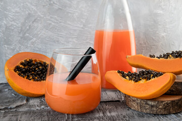 Papaya juice or smoothie in glass with pieces of papaya organic fruit around on wooden table. Still life photo. Superfood nutrition concept. Detox exotic beverage.