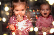 © Maria - Family holidays at home. Two happy kids holding burning sparkler, indoor lifestyle