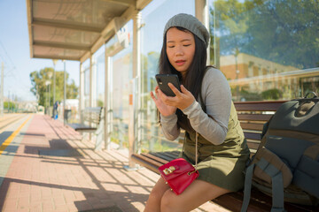 Canvas Print - outdoors lifestyle portrait of young beautiful and happy Asian Japanese woman waiting the train sitting on station platform bench using mobile phone checking schedule online