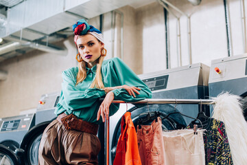 Wall Mural - young stylish woman in turban standing near washing machines in laundromat