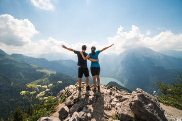 Girl and boy standing on the top of a cliff holding each other and spreading arms, beautiful scenery in the background