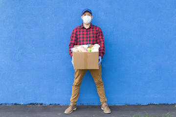 Wall Mural - volunteer with a box of food on a blue background, donations