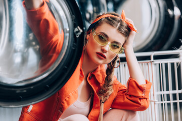 Wall Mural - young woman in sunglasses sitting washing machines with blurred foreground