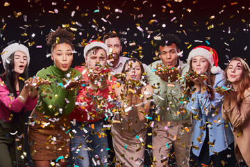 Celebrating New Year 2021 together. Group of young multiracial happy people blowing colorful confetti