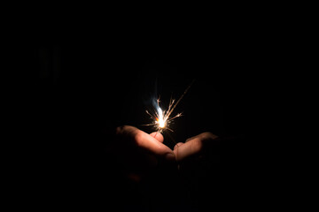 Two sparklers gathered together and emerging from the dark, are almost burned out to the end.