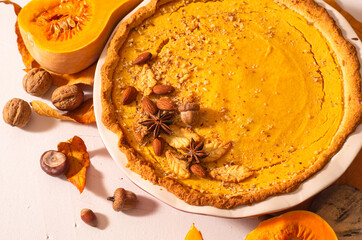 Sweet pumpkin pie decorated with nuts and cinnamon and slice pumpkit, on white table with dry leafs