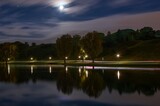 Fototapeta  - Long exposure of city lights and clouds in a park at night. Long exposure of light reflections in a lake in Munich at night.