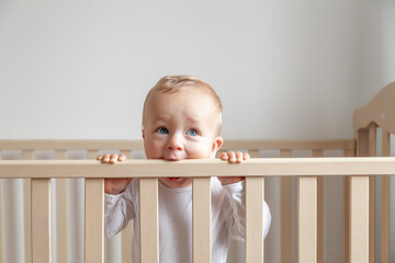 Blond cute little baby biting wooden bed headboard