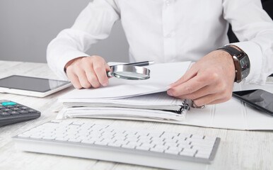 Poster - Man holding magnifying glass with documents.