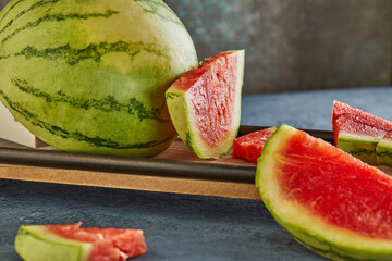 Sticker - Mini Watermelon with sliced wedges on a wooden stand on a blue background