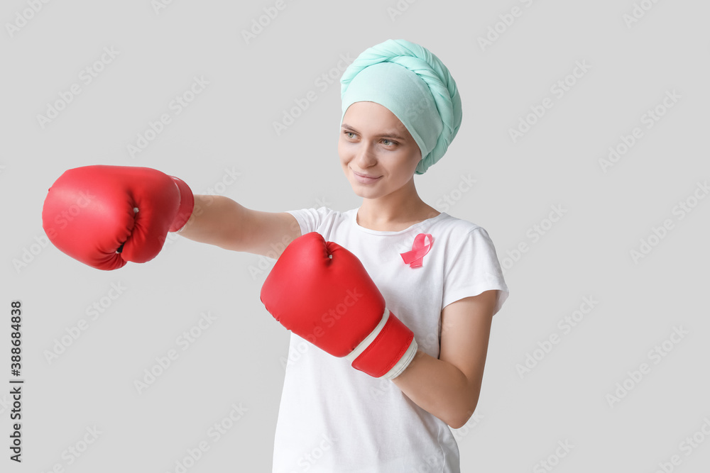 Woman after chemotherapy in boxing gloves on grey background. Breast cancer awareness