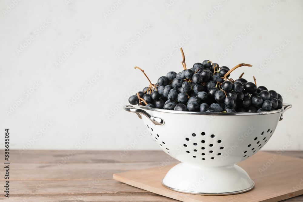 Colander with sweet ripe grapes on table