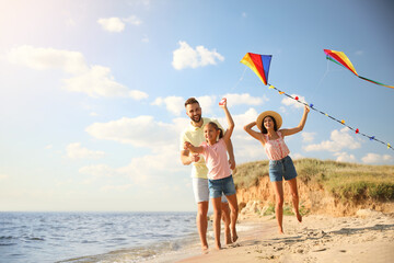 Canvas Print - Happy parents and their child playing with kites on beach near sea. Spending time in nature