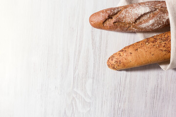 Two fresh baguettes with whole grain and seeds. White wooden background. Top view.