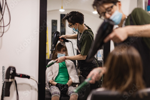 Hairdresser and girl child customer in a salon with medical masks during virus pandemic. Working with safety mask.