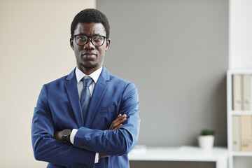 Wall Mural - Portrait of African young businessman in eyeglasses and in formalwear standing with his arms crossed and looking at camera