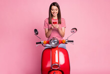 Photo Portrait Of Surprised Woman Sitting On Red Moped Texting On Smartphone Smiling Isolated On Pastel Pink Color Background