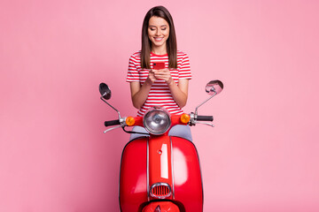 Sticker - Photo portrait of surprised woman sitting on red moped texting on smartphone smiling isolated on pastel pink color background