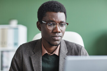 Wall Mural - African manager in eyeglasses looking at monitor of laptop during his work at office