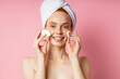 © liliyabatyrova - Pretty glad young caucasian woman with towel on head, bare shoulders, holding two cosmetic sponges on cheeks, enjoying beauty day smiling broadly posing against pink studio wall. Skin care.