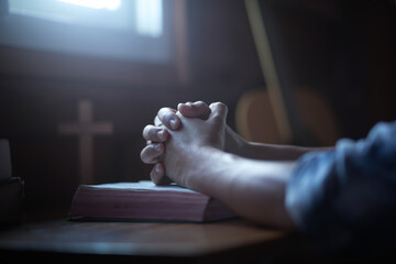 Wall Mural - Close up hands praying on holy bible on wooden table in morning. Christian worship concept.