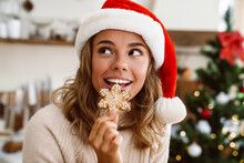 Happy Cute Woman In Santa Claus Hat Smiling And Eating Christmas Cookie