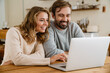 © Drobot Dean - Beautiful happy couple using laptop while sitting in kitchen
