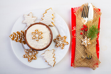 Knife, fork and plate with gingerbread cookies with New Year's decor on a white table top view.