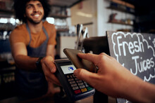 Closeup of young female hand making contactless payment in cafe using smartphone with waiter holding machine