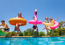 Group Of Happy Little Kids Dive In Water With Inflatable Toys Flamingo Doughnut Jump Into The Swimming Pool