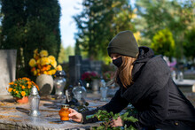 A Woman Wearing A Protective Mask Against The Coronavirus In The Cemetery, Holding A Candle Snitch In A Hand. A Woman In A Cemetery During A Pandemic. Covid On All Saints. Restrictions On The Cemetery