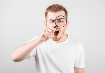 Shocked man looking in magnifier on grey background