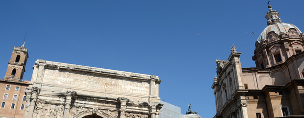 In the center of Rome, the ancient Roman Forum with the Septimius Severus Arch and the Baroque facade of the Saints Luca e Martina church.