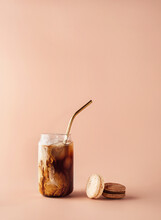 Glass Of Iced Coffee In Tall Glass With Golden Straw With Cream And Macaroons Chocolate, Vanilla On Pastel Background For Your Design. Food Concept In Vintage Style. Copy Space. Closeup.