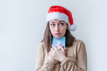 Wall Mural - Beautiful girl in red Santa Claus hat holding blue gift box in hand isolated on white background. Young woman portrait, true emotions. Happy Christmas and New Year holidays concept.