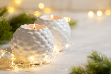 Two white candlesticks with burning canles flame with garland lights. Christmas decoration