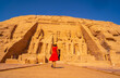 © unai - A European tourist in red dress walking towards the Abu Simbel Temple in southern Egypt in Nubia next to Lake Nasser. Temple of Pharaoh Ramses II, travel lifestyle