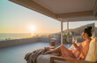 © Trevor Adeline/Caia Image - Woman enjoying white wine and sunset ocean view on luxury balcony