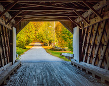 Looking From The Inside Of A Historic New England Covered Bridge Out At Road Covered In Fall Foliage Colored Trees
