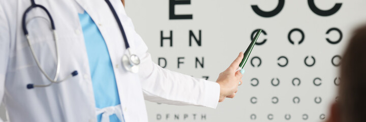 Close-up of professional ophthalmologist checking vision of patient. Experienced oculist pointing to letter in vision test table. Healthcare and prevention concept