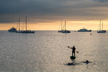 Paddle Boarding During The Sunset At Puerto Barquerizo Moreno Beach In San Cristobal Island,  Galapagos Islands, Ecuador.
Multiple Sailboats Can Be See At The Background.