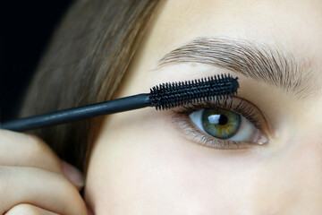 Close up of beautiful face of young woman getting make-up. a young woman applying a mascara to her eyelashes on a dark background.