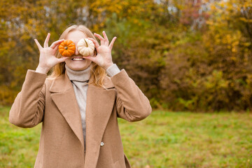 The girl covers part of her face with an orange and white pumpkins. Harvest concept. Copy space. Autumn lifestyle. Smiling Woman being playful covering her eyes with pumpkins