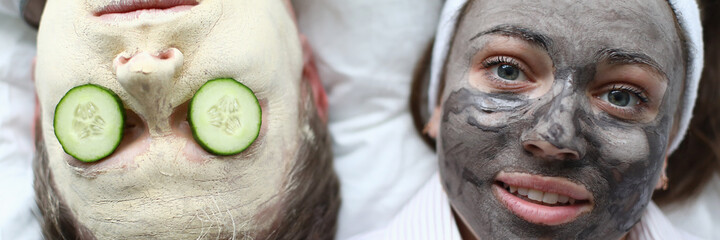 Wall Mural - Top view of woman and man wearing cleaning face masks. Relaxed female and male laying on sofa. Couple with cucumber slices on eyes. Spare time at home and cosmetology concept