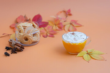 Pumpkin spice latte in a glass mug with whipped cream on  beige background. Autumn leaves. Hot autumn drink.