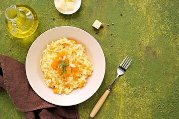 Vegetarian pumpkin risotto in a beige ceramic plate on a green concrete background. Italian food. Pumpkin recipes.